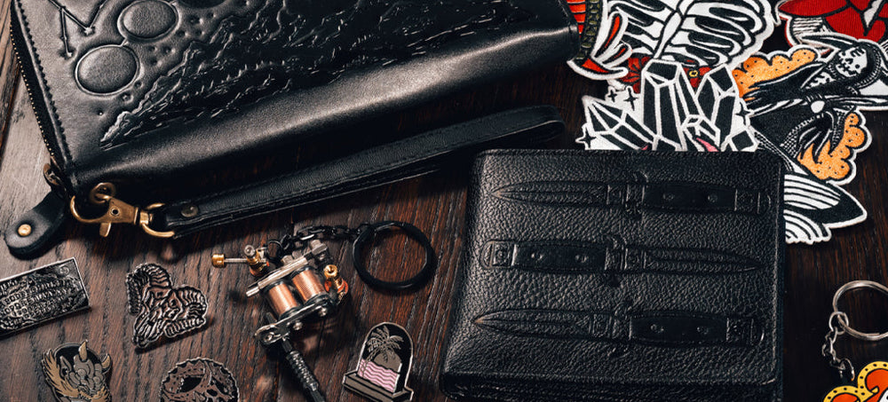 A black wallet and leather pouch set on a brown wooden table with edgy stickers.