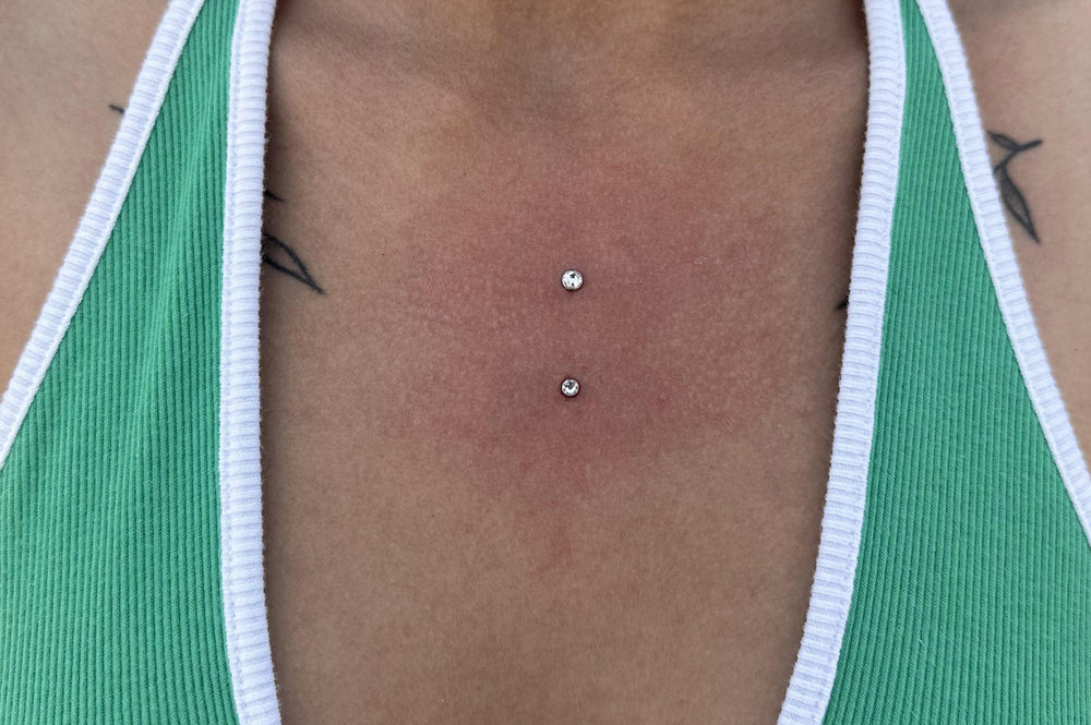 A women wearing a green bikini top, showing her chest dermal piercing in the centre of her chest