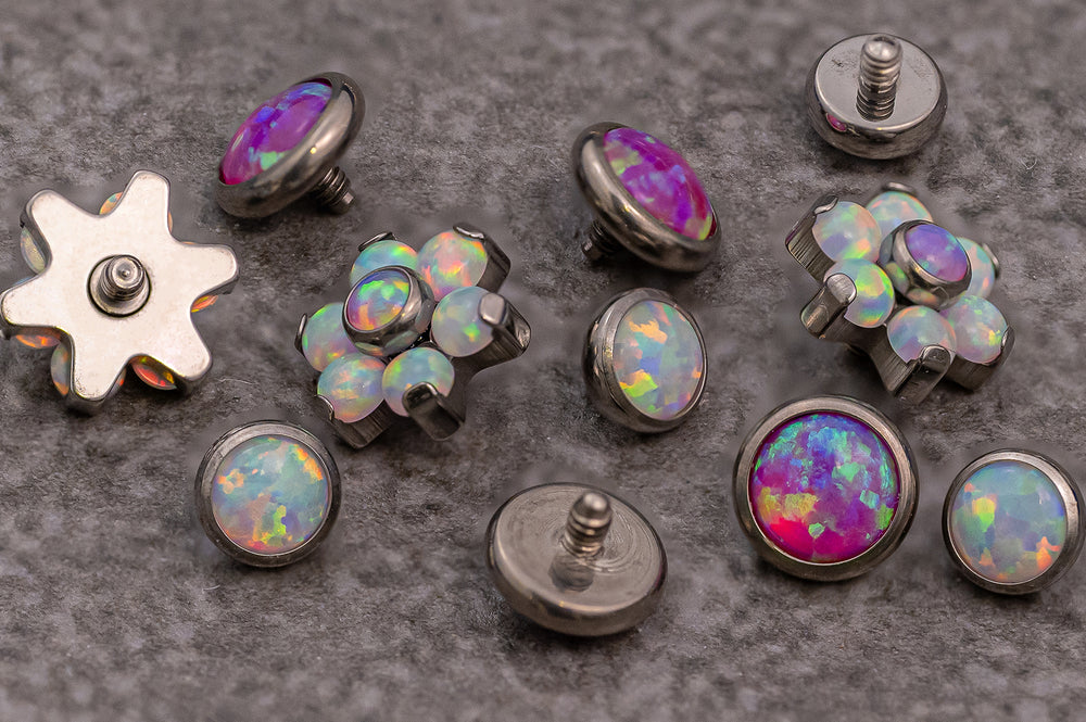 A variety of shaped shiny purple and iridescent dermal anchor piercings on a stone worktop