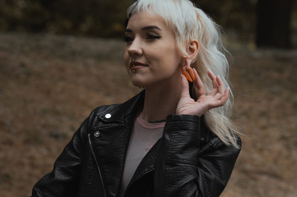 A women smiling and showing her new Custom Plugs ear weight whilst out on a walk.