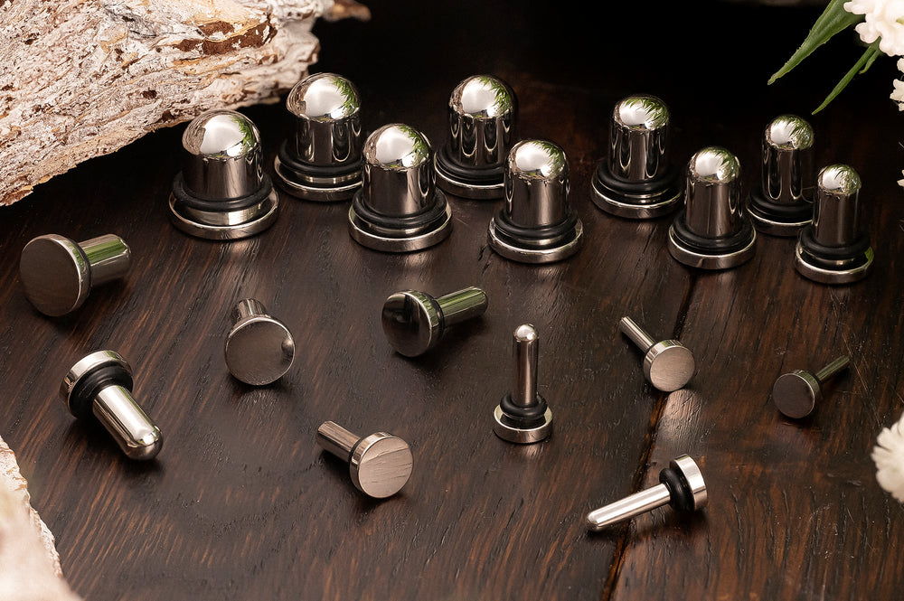 A variety of sized metal ear plugs for dead stretching,  displayed on a rustic wooden board