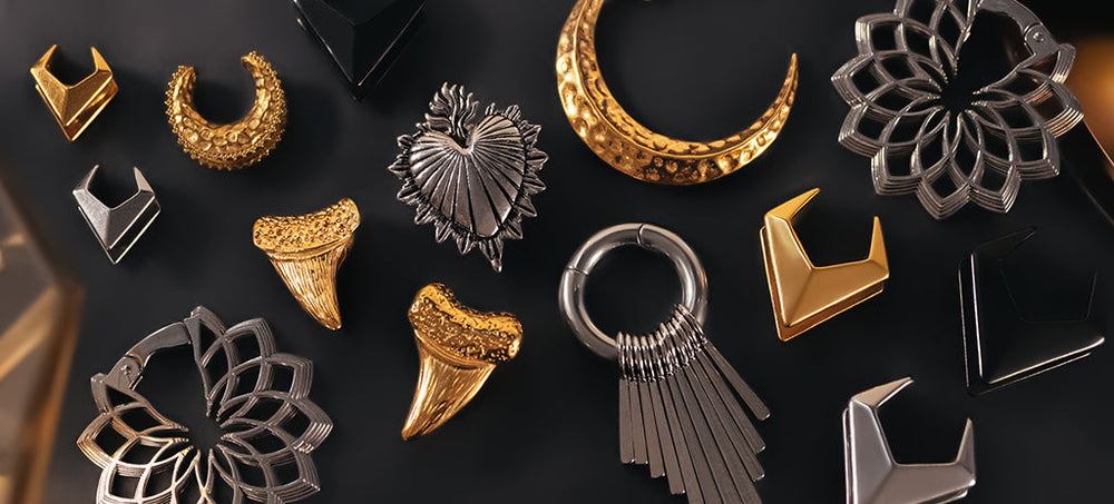 A collection of silver and gold metal ear weights, set on a black background.