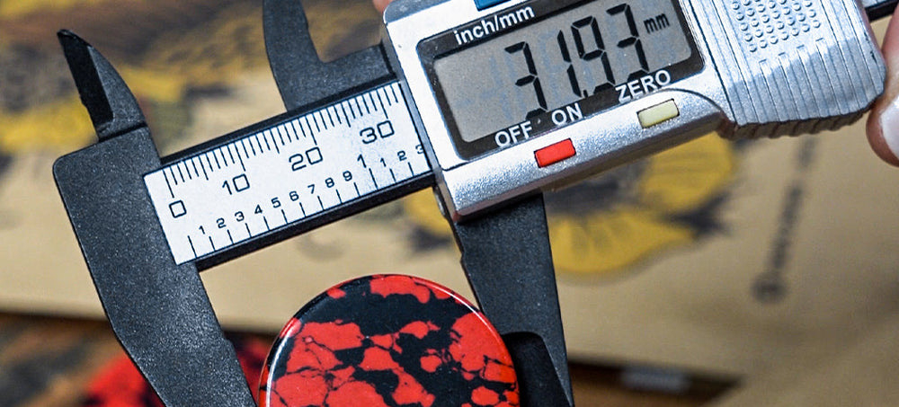 A picture of a measuring tool, that is measuring a red and black marbled ear gauge.