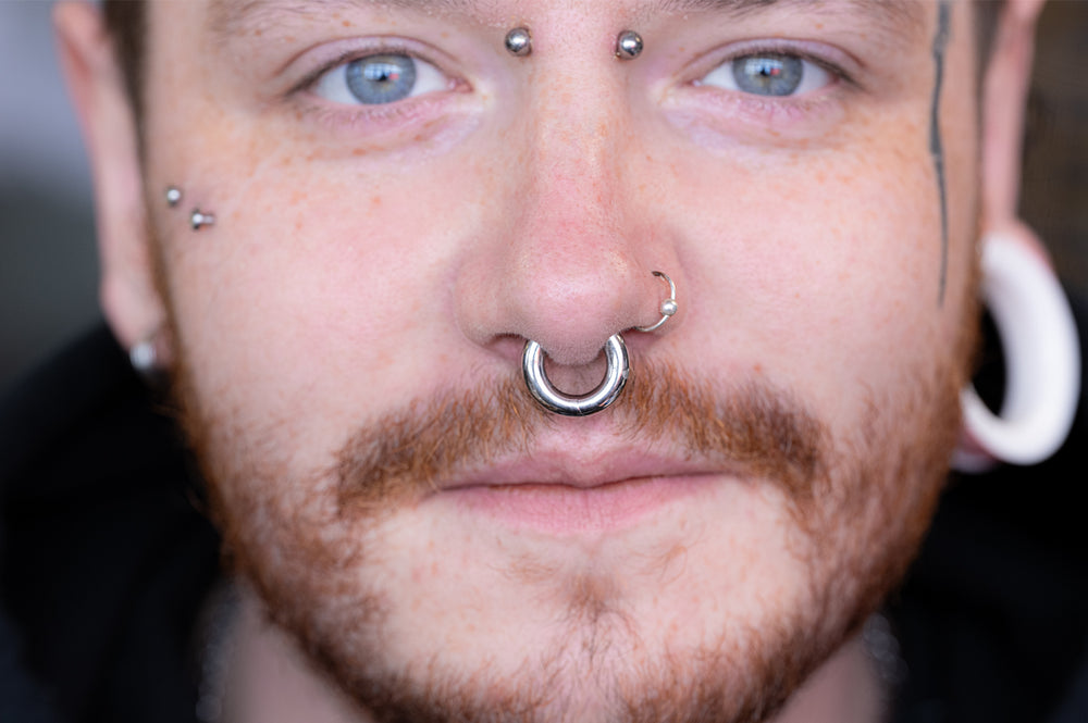 A man with a beard and stretched ears and multiple body piercings, including a stretched septum