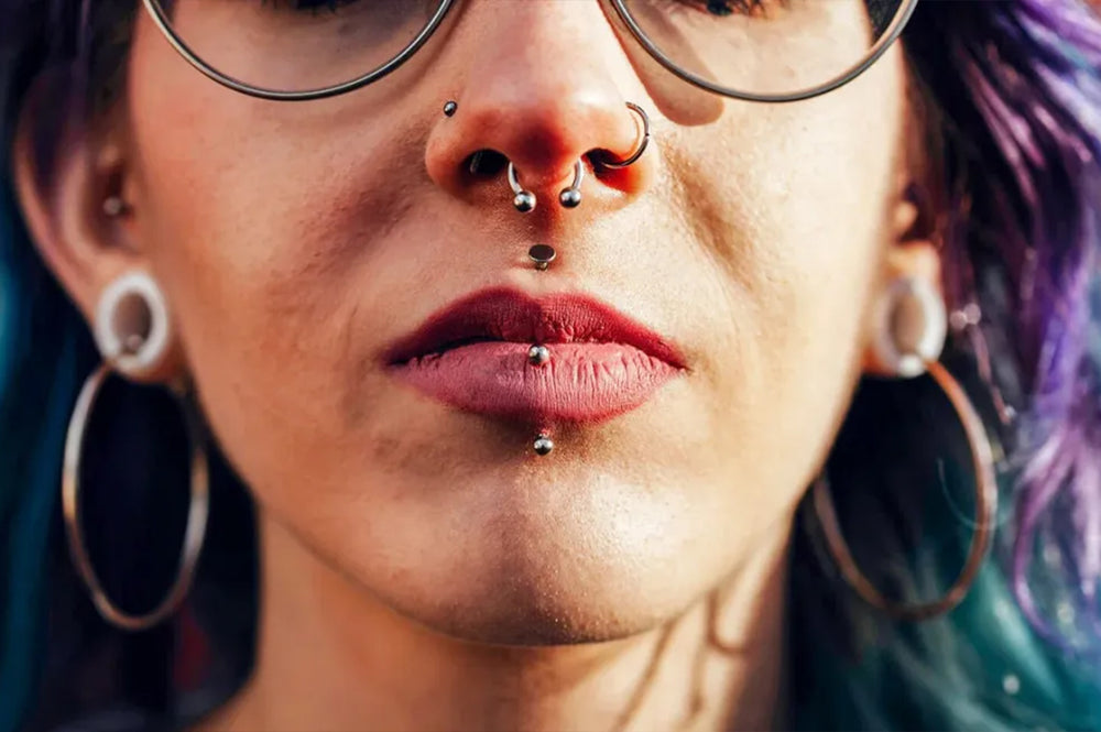 A women showing her labret piercing and nose piercings - she has stretched ears with dyed purple hair.
