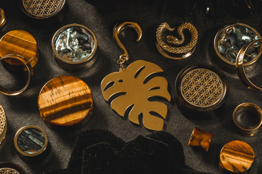 A variety of gold wood, glass and metal ear plugs and ear hangers, displayed on a black background