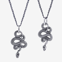 Deux pendentifs en forme de serpent sur des chaînes, sur fond blanc